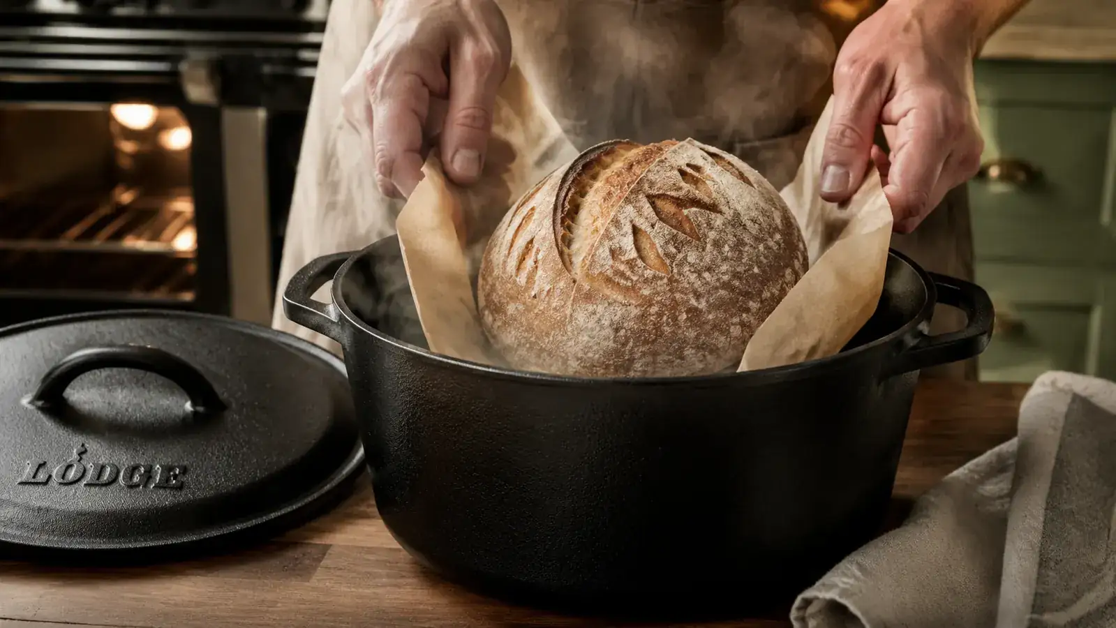 Hands lowering a sourdough boule on parchment paper into a preheated Lodge Double Dutch Oven